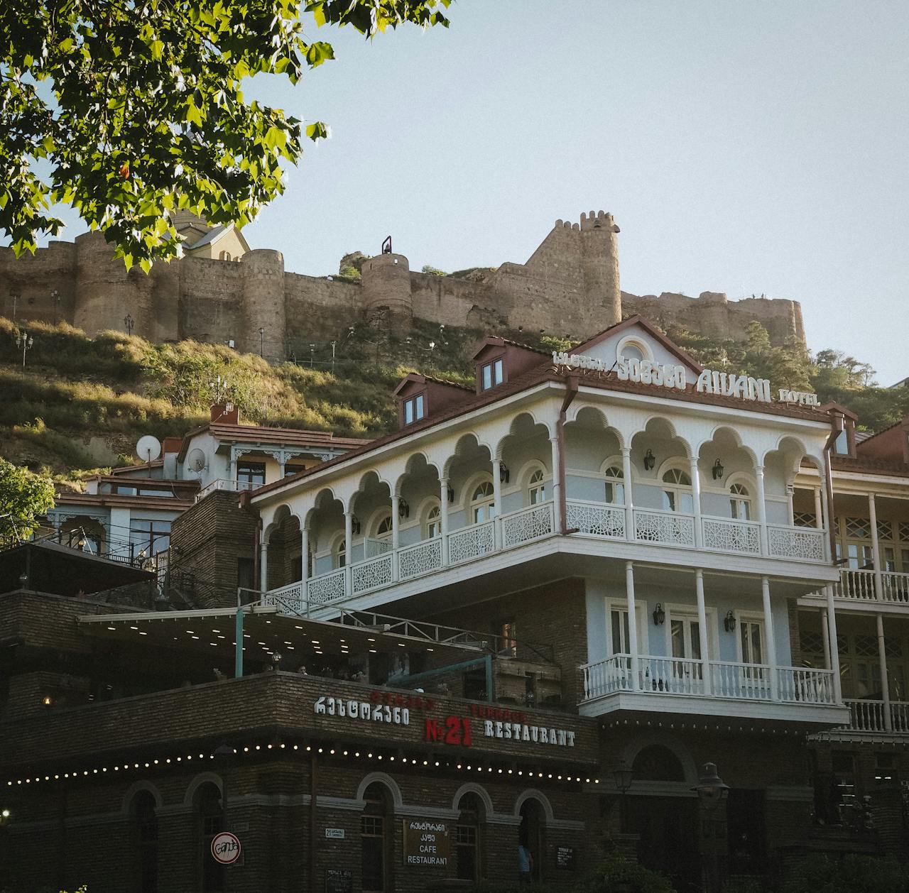 View of Narikala Fortress atop a hill with a traditional hotel in Tbilisi, Georgia.